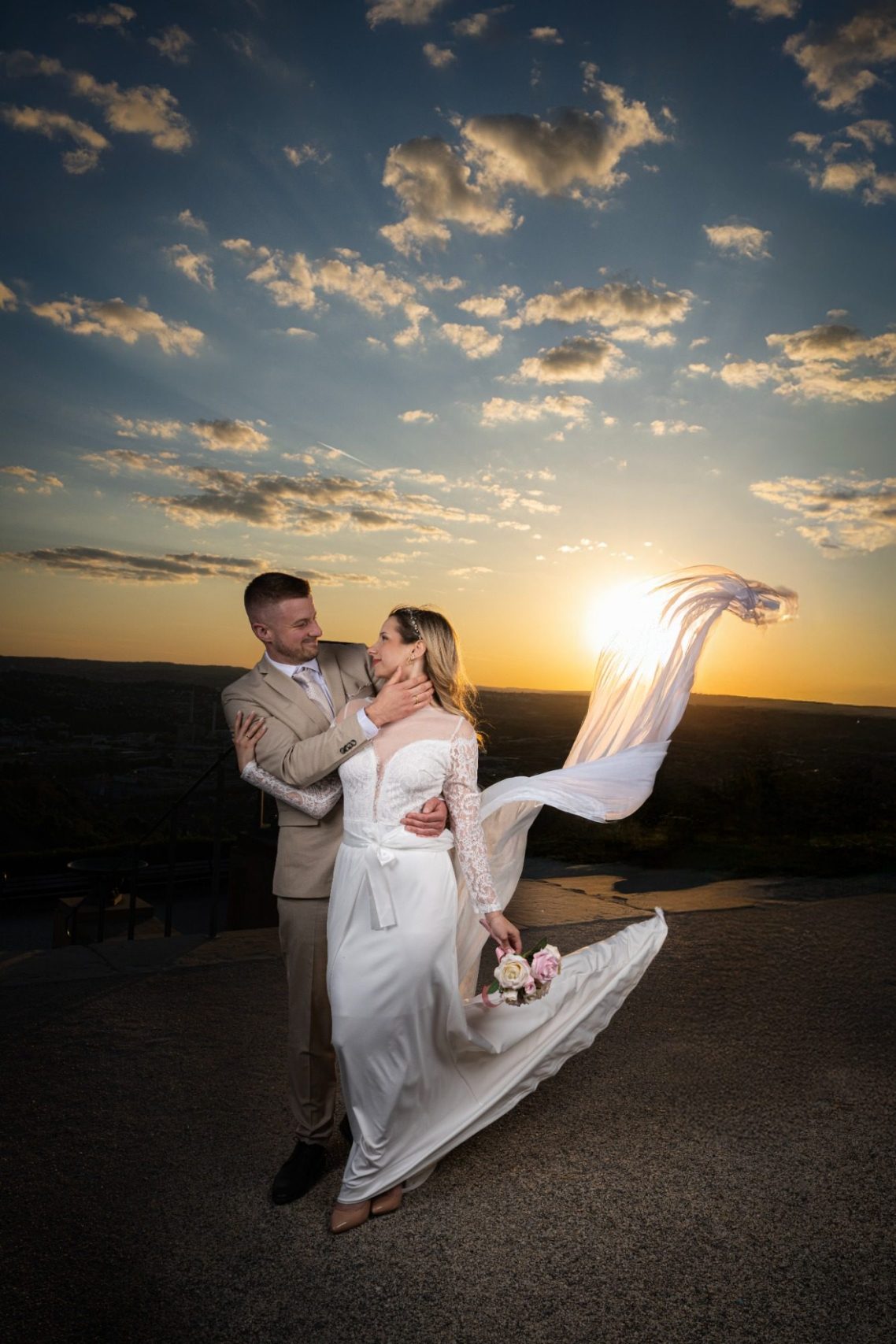 Sunset Ein Brautpaar küsst sich vor dramatischem Himmel in einem Garten.